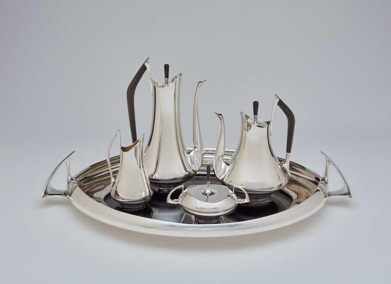Elegant silver tea set on an oval tray, featuring five sleek, modern teapots with dark handles
